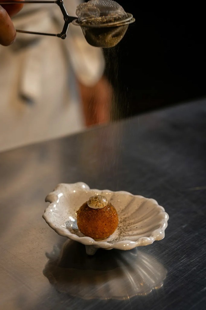 A pastry in a shell dish as a fine powder is dusted over it with a sieve.