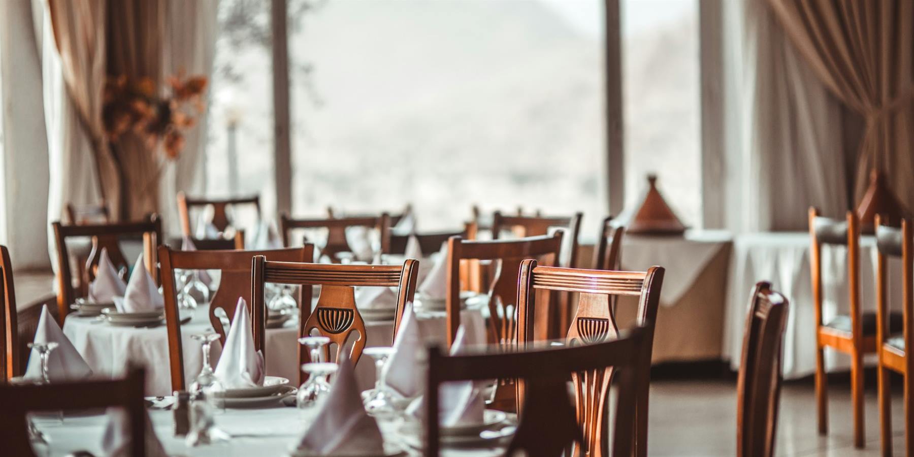 A dining room set with white linen, wooden chairs and glassware.