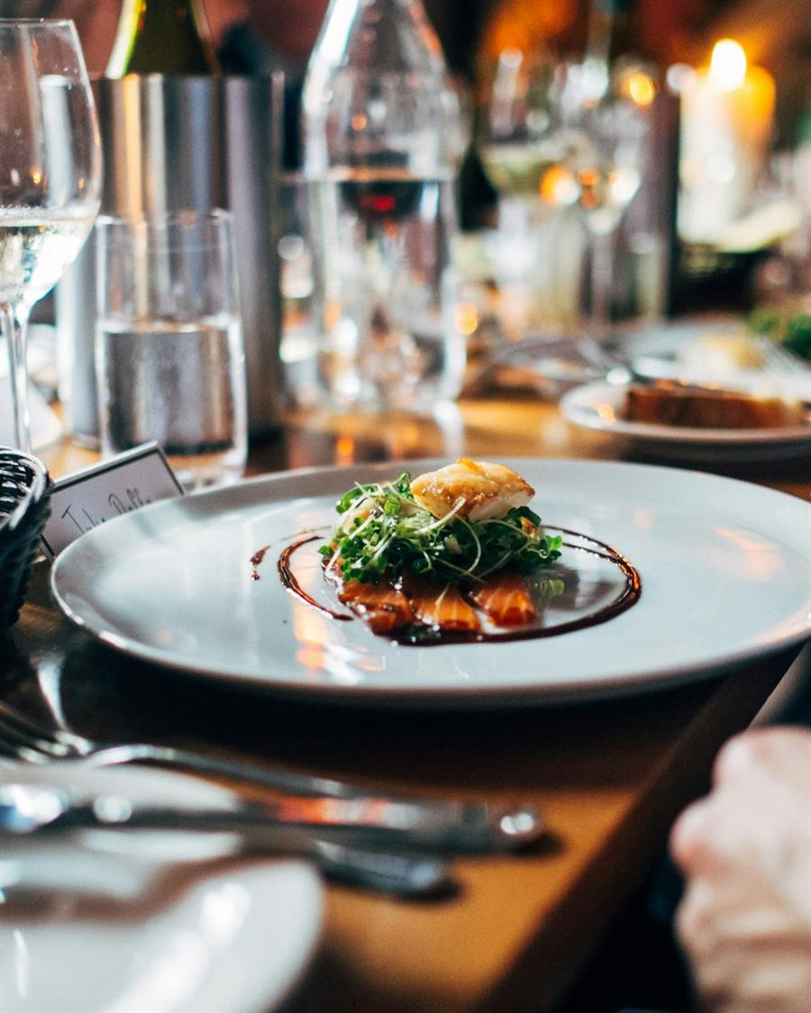 Illustrative image: a plated dish on a restaurant table, with wine glasses beyond.